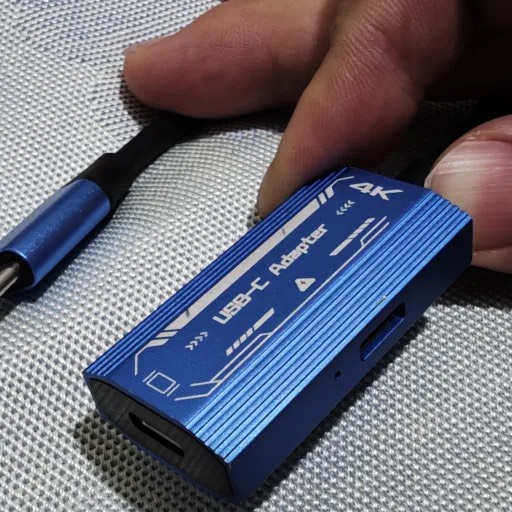 Blue 4K HDMI-to-USB-C adapter held in one hand